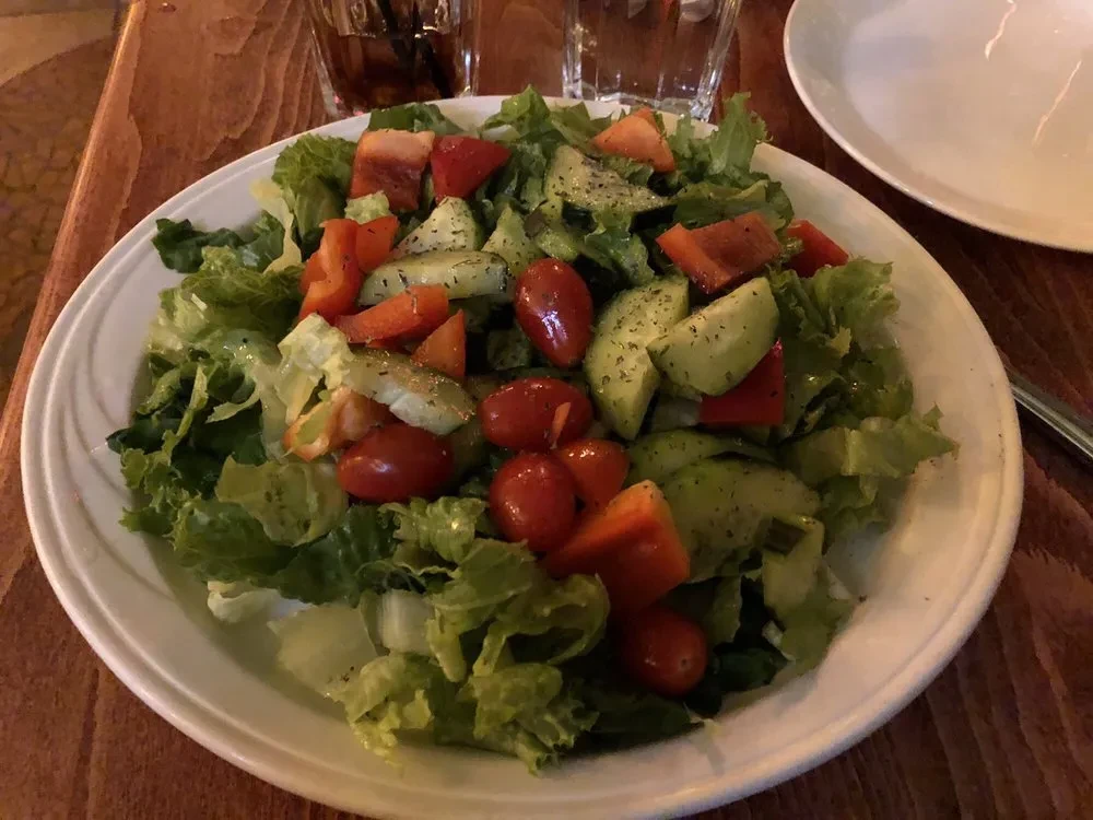 Fresh salad on a white plate with lettuce, tomatoes, cucumbers, peppers.