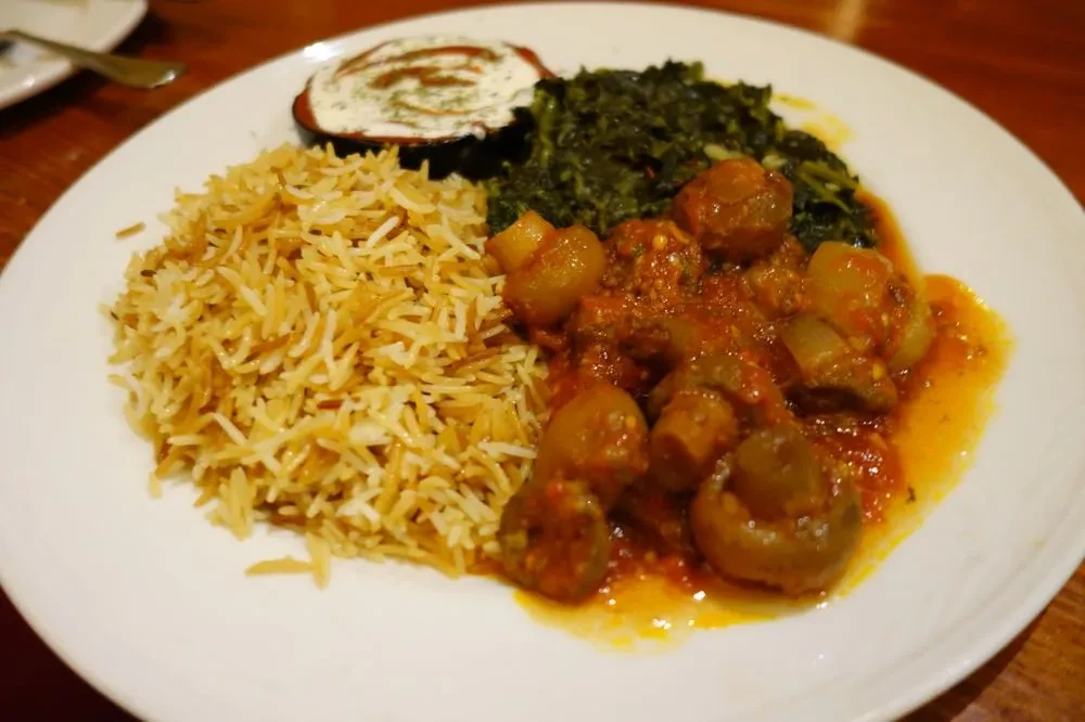 Plate with basmati rice, leafy greens, rich stew, and creamy dip.
