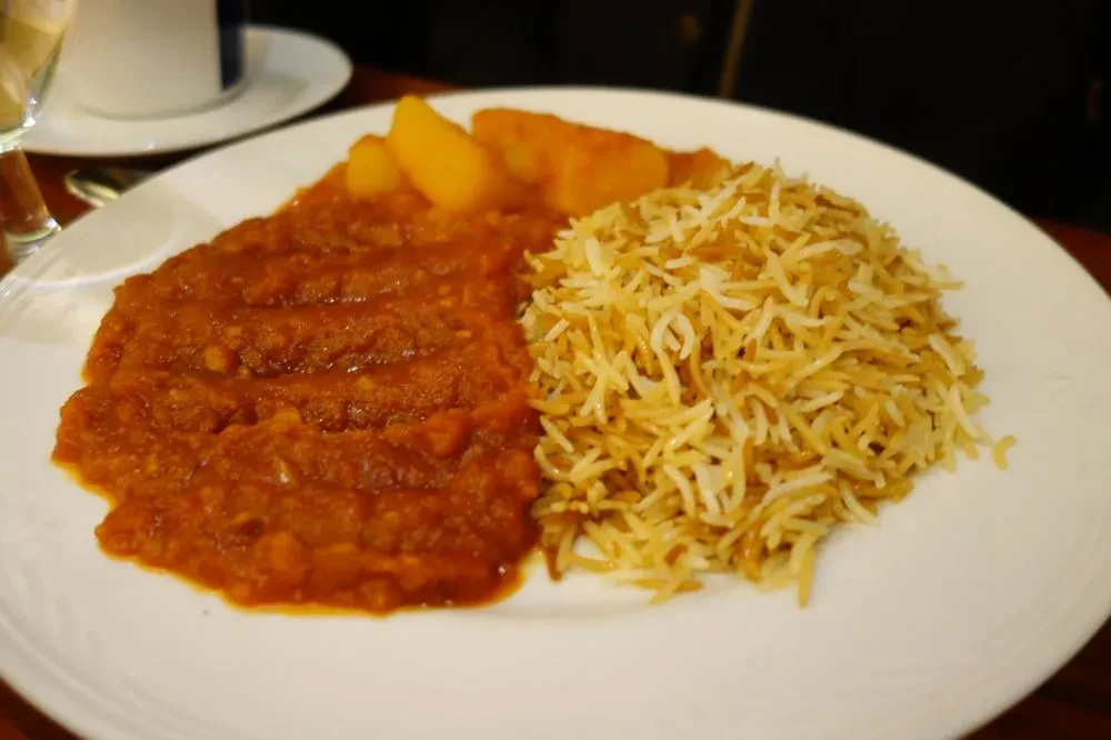 Reddish stew with potatoes and fluffy basmati rice on a white plate.