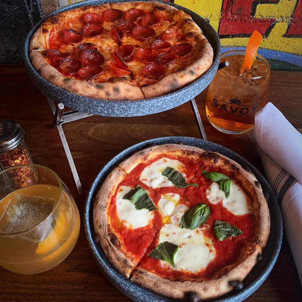 Overhead shot of pepperoni and Margherita pizzas and two cocktails.