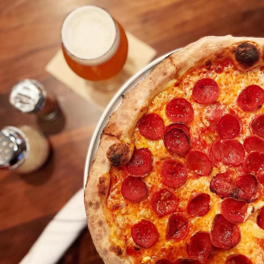 Freshly baked pepperoni pizza and beer on a wooden table.