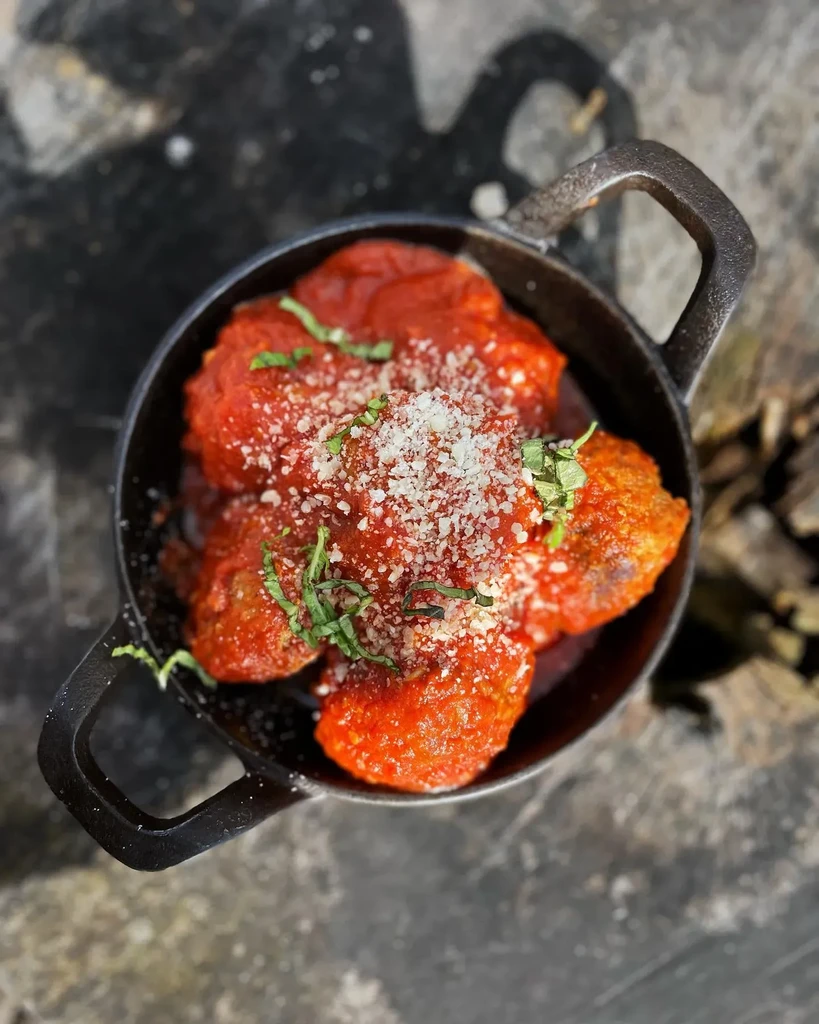 Rustic pot with meatballs in red sauce, cheese, and herbs.
