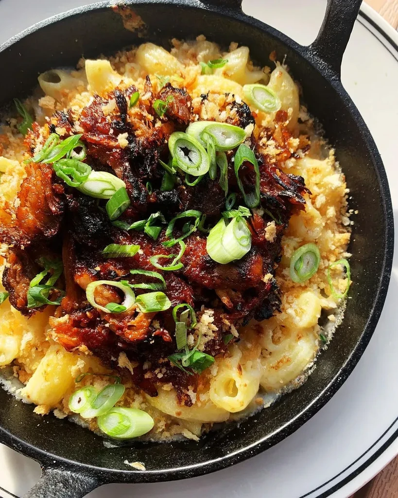 Skillet mac and cheese topped with braised meat, breadcrumbs, and green onions.