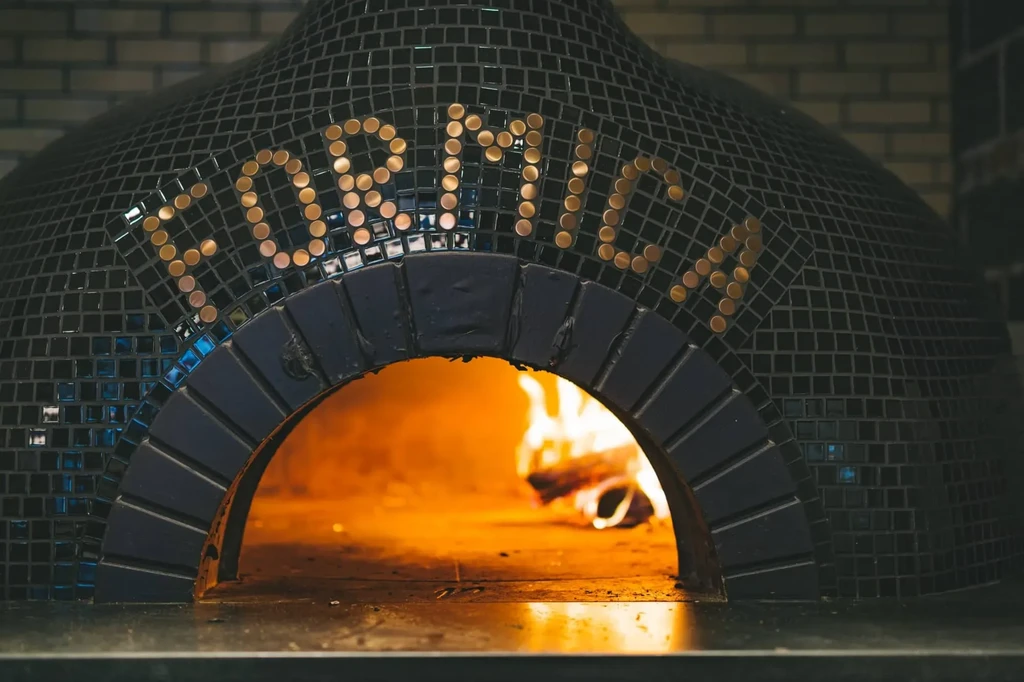 Dark mosaic wood-fired pizza oven with "FORMICA" logo and active flames.