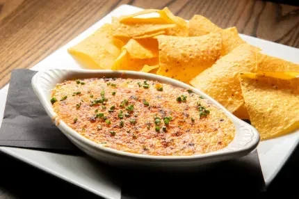 Baked cheese dip with herbs and tortilla chips on a white plate.