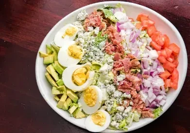 Large salad with hard-boiled eggs, avocado, blue cheese, and bacon.