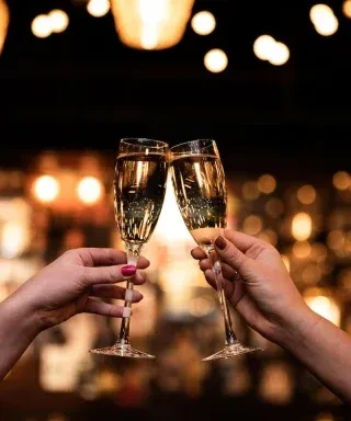 Hands with red and neutral nails clinking golden champagne flutes.