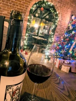 Wine bottle, glass on table, festive brick archway and Christmas tree.