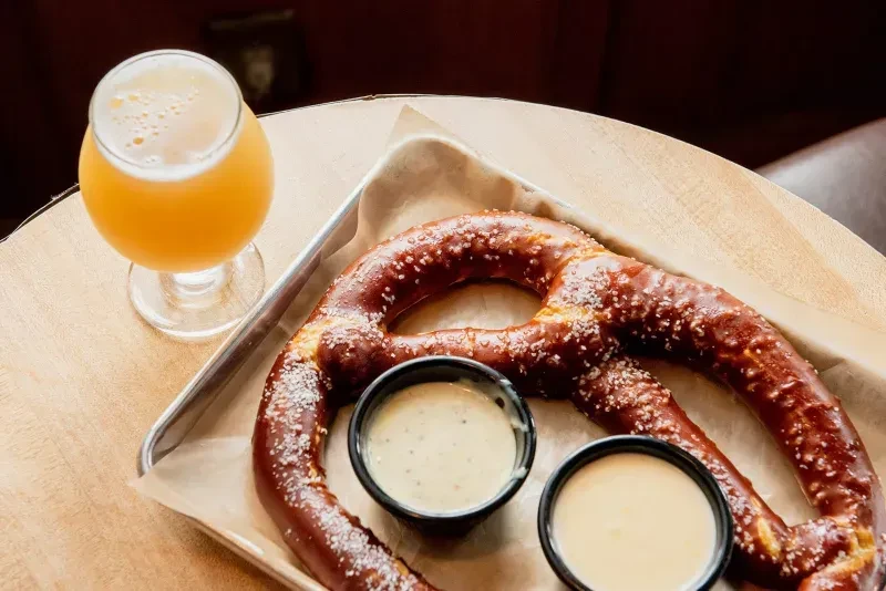 Large salted pretzel, cheese and mustard dips, and craft beer.
