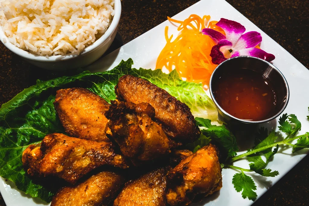 Plated fried chicken wings, rice, dipping sauce, lettuce, and orchid garnish.
