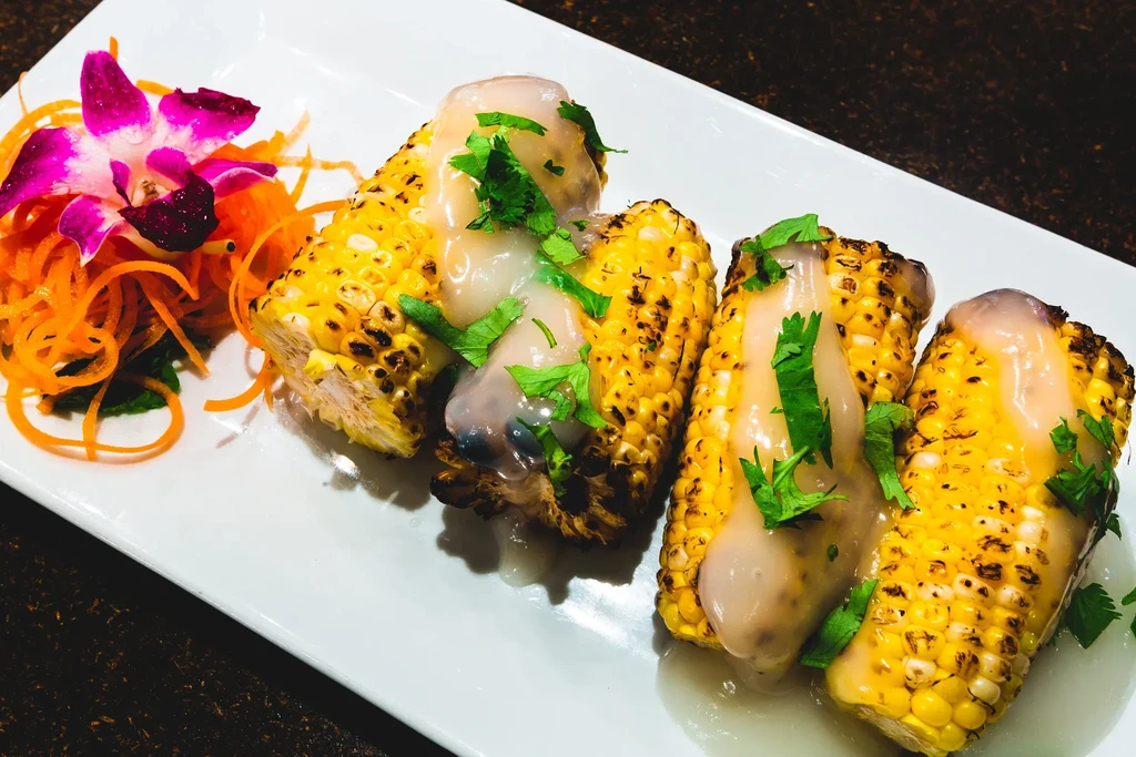 Four grilled corn on the cob with sauce, cilantro, carrots, orchid.