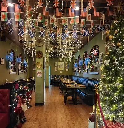 Empty British pub interior decorated for Christmas with lights, flags, and tree.