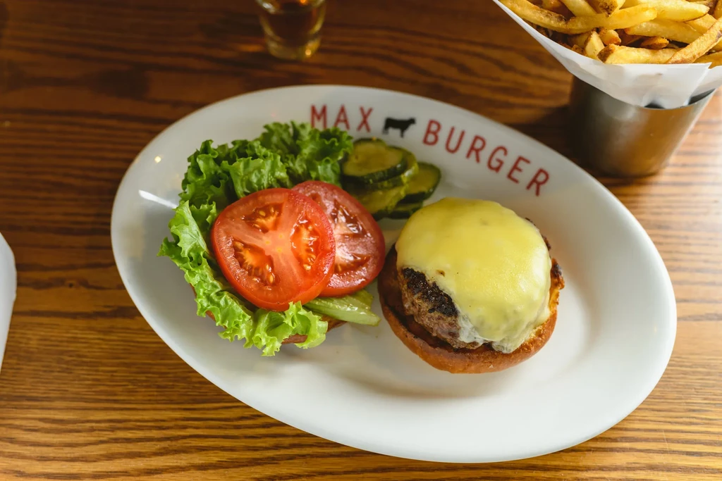 Deconstructed cheeseburger, fries, and drink on a Max Burger branded plate.