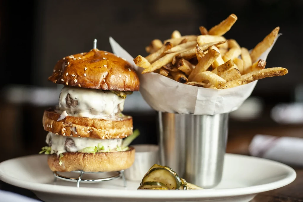 Close-up of double-patty burger, melted cheese, lettuce, fries, and pickles.