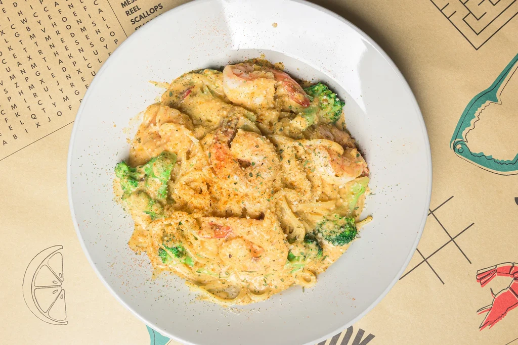 Close-up of creamy shrimp and broccoli pasta on a graphic paper placemat.