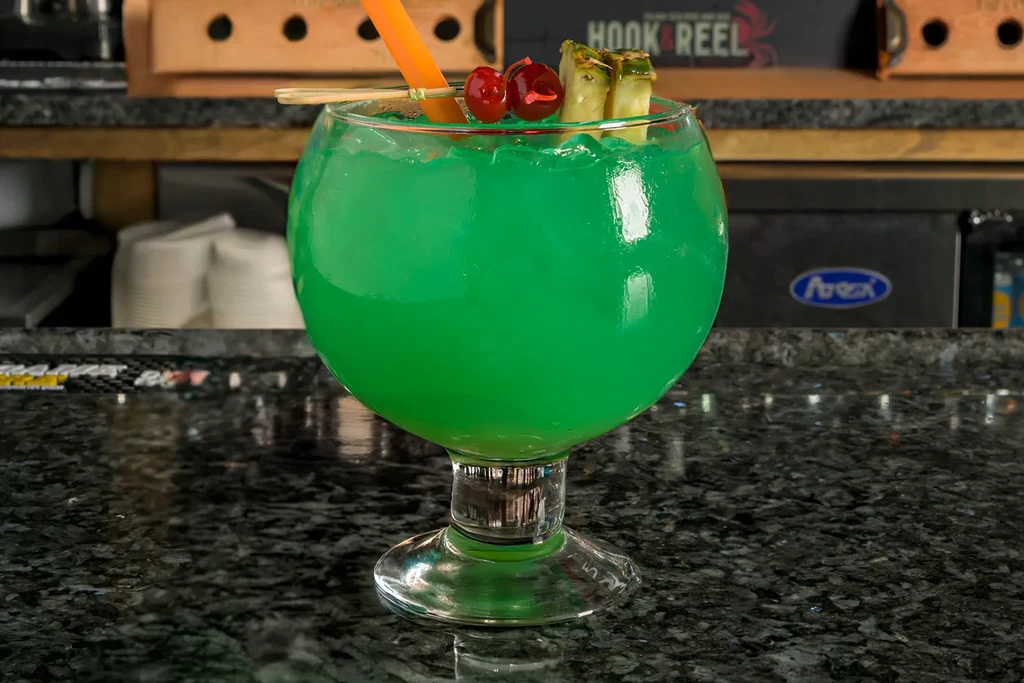 Vibrant green cocktail with cherries and pineapple on a bar.