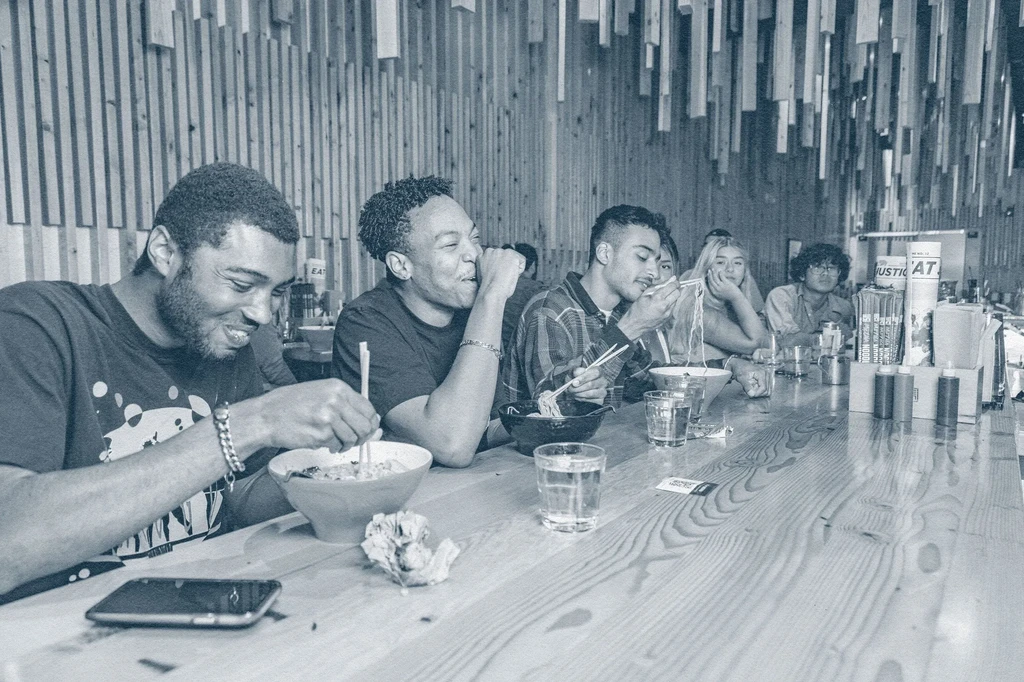 Young adults eating ramen and laughing at a modern counter.