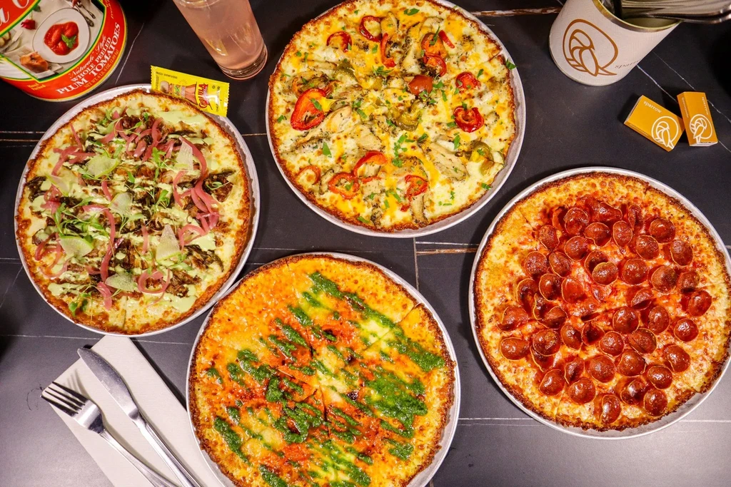 Flat lay of four distinct pizzas on a dark tabletop.