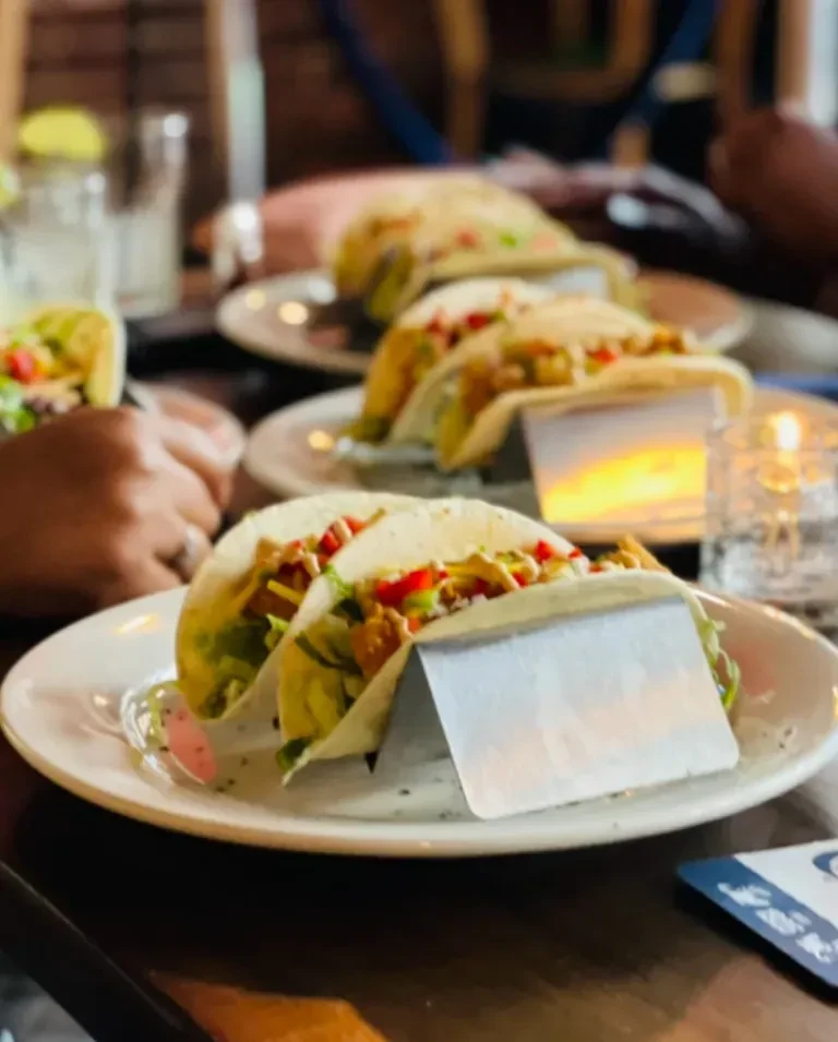 Tacos in holders, drinks, and a candle on a dim restaurant table.