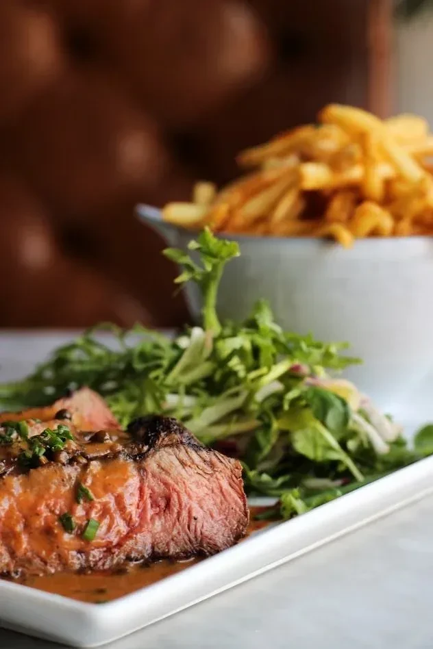 Sliced medium-rare steak with sauce, green salad, and french fries.