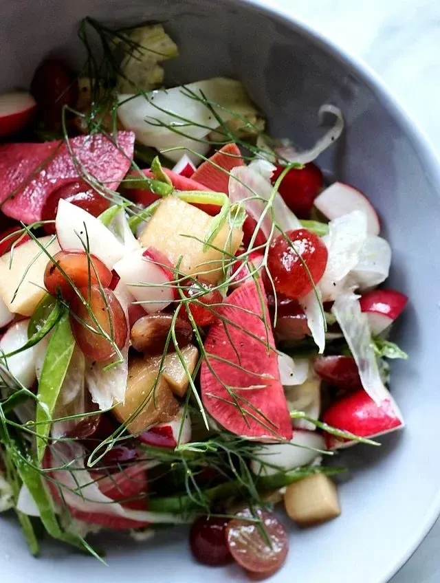 Close-up of a vibrant salad with radishes, grapes, and green fennel.
