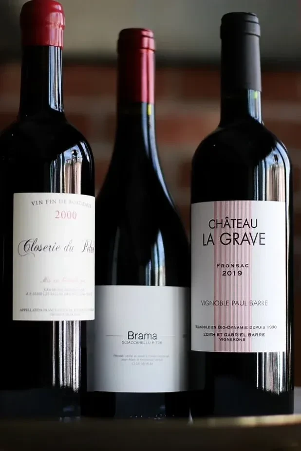 Three dark wine bottles with distinct, legible labels, blurred cellar background.
