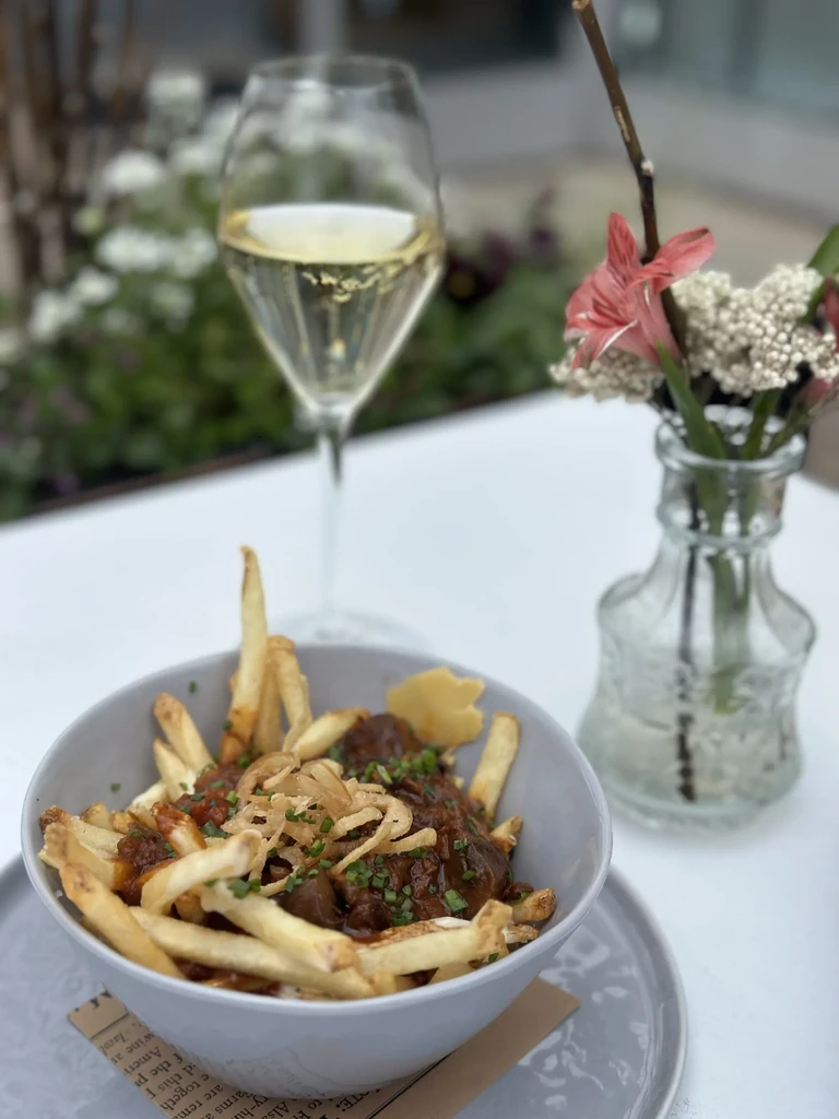 Close-up poutine garnished with chives and fried onions, flowers, sparkling drink.