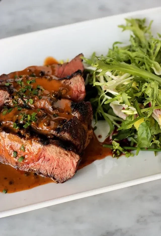 Sliced medium-rare steak with sauce, herbs, and a fresh green salad.