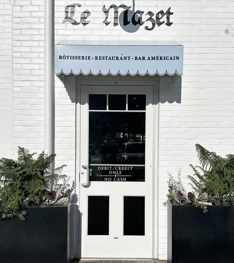 Le Mazet restaurant exterior with white door, blue awning, and planters.