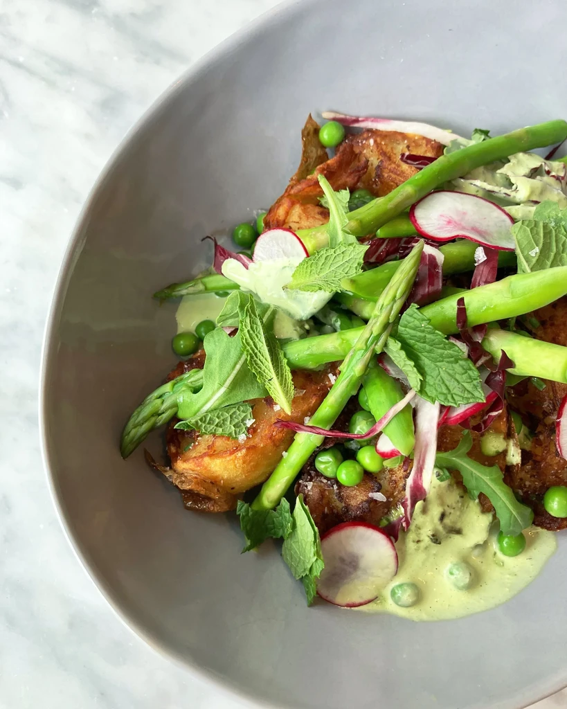 Beautifully plated potatoes, asparagus, peas, radishes, and mixed greens.