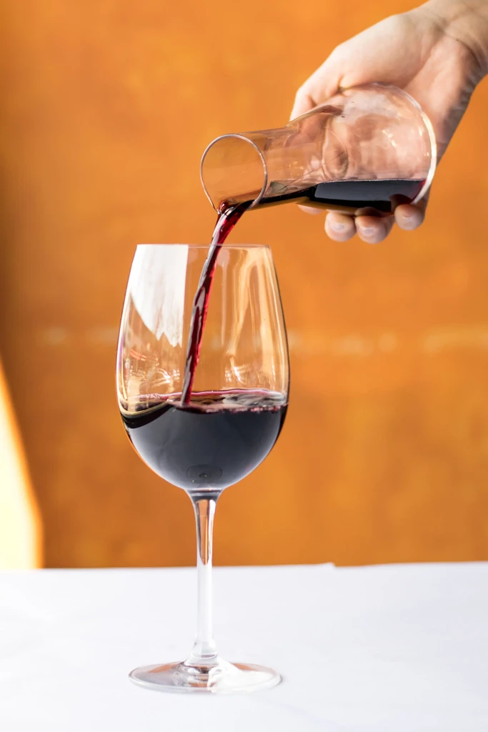 Red wine pours from a carafe into a clear stemmed glass.