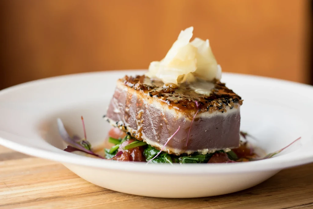 Seared tuna with sesame crust, dark glaze, ginger flakes, and greens.