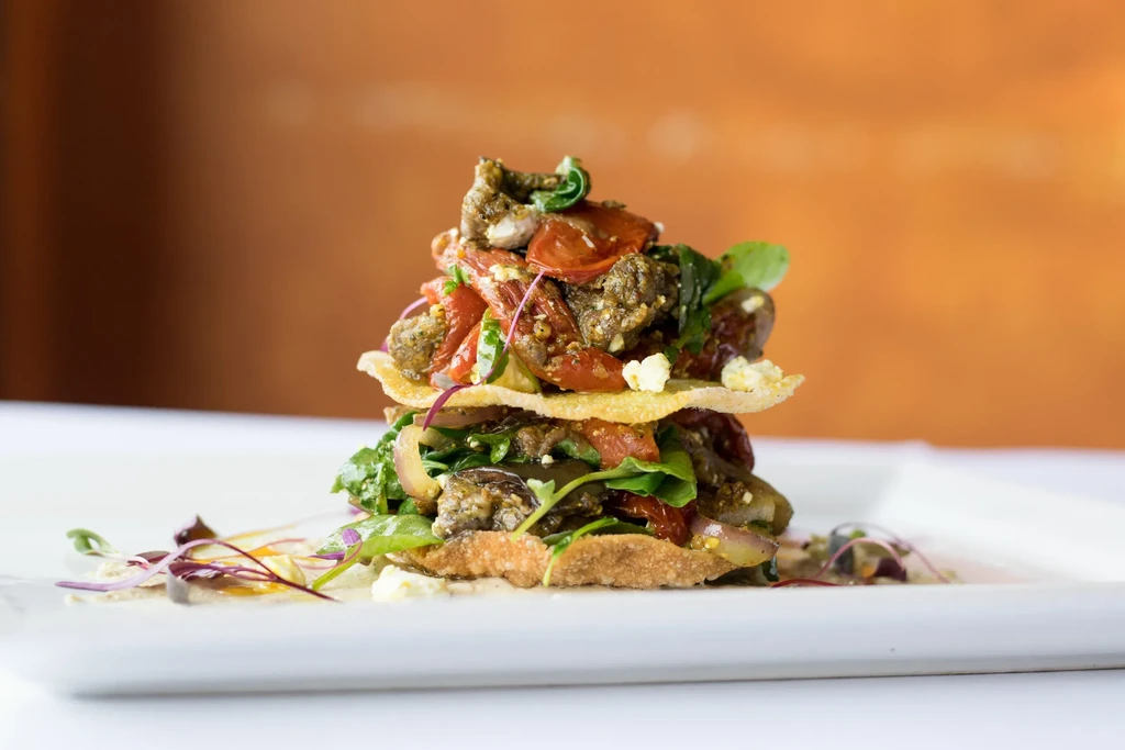 Plated tower of flatbread, greens, protein, and cheese.