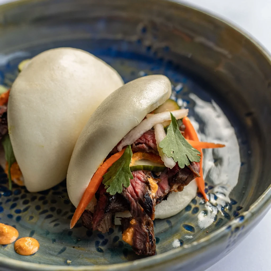 Two open-faced bao buns with meat, carrots, daikon, cilantro, orange sauce.