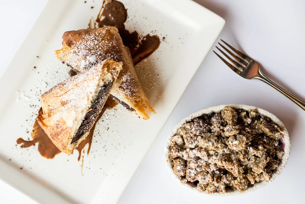 Two triangular pastries with dark filling, a crumble, powdered sugar.