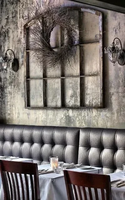 Restaurant interior showing distressed wall, antique window with wreath, and dining booth.