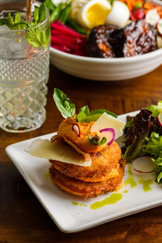 Plated fried appetizer, sparkling cocktail, and blurred meal on wood table.