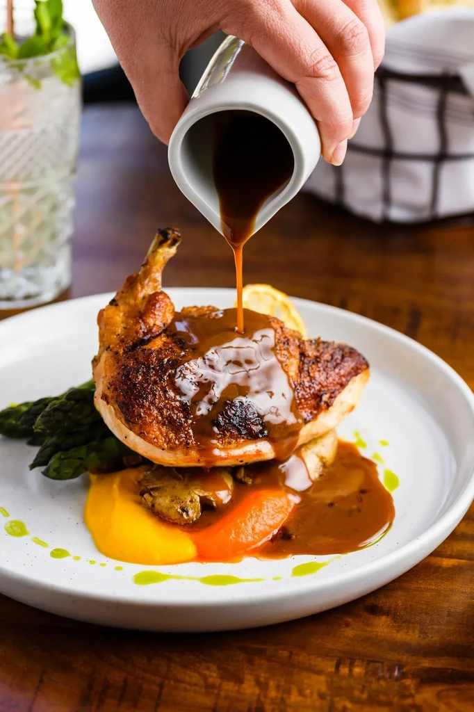 Hand drizzles sauce over roasted chicken, puree, asparagus, and mushrooms.