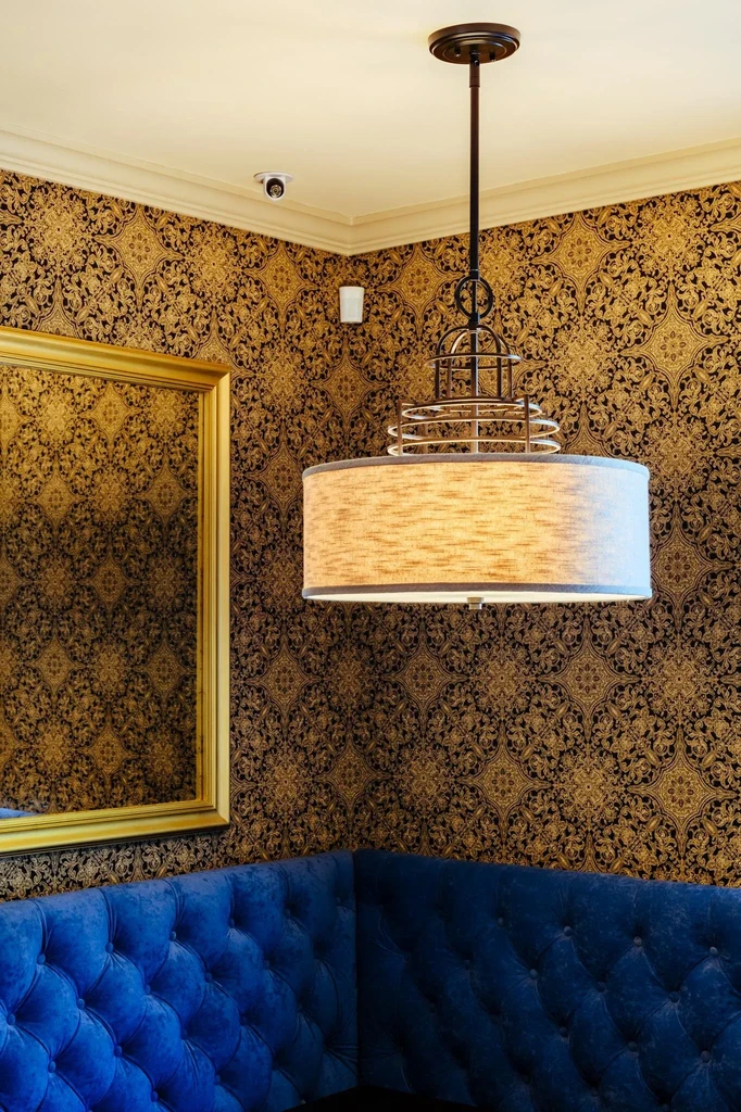 Restaurant corner: gold patterned wallpaper, blue booth, beige light, and mirror.