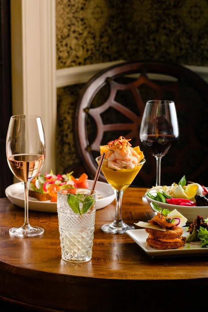 Gourmet food and cocktails on a dark wood table in a restaurant.