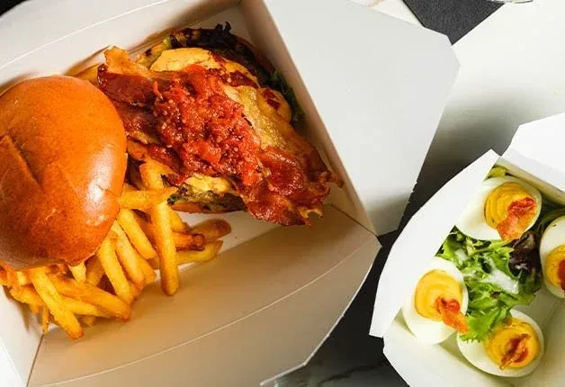 Takeout burger with bacon, fries, and salad with eggs. Top-down.