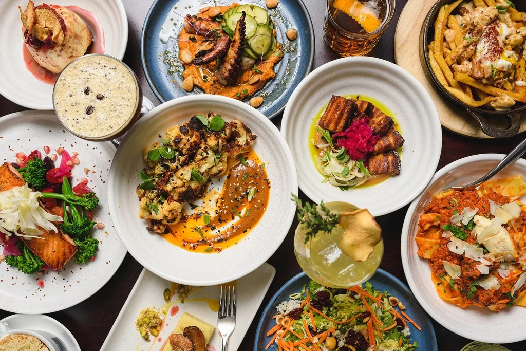 Vibrant overhead flat lay of diverse gourmet food and cocktails.