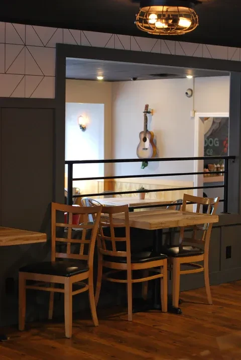 Cozy restaurant interior with wooden chairs, pass-through, and guitar on wall.