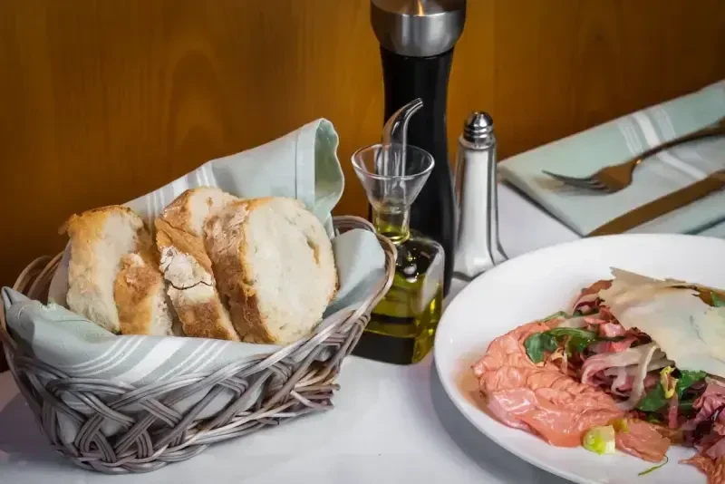 Close-up of a dining table with bread, condiments, and carpaccio appetizer.