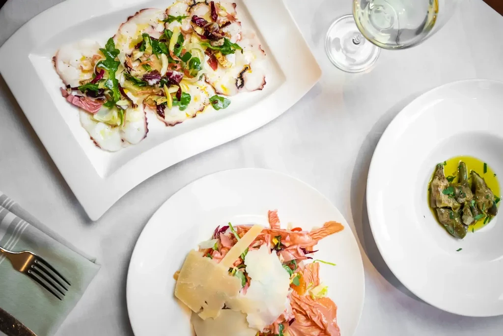 Overhead shot of dining table set with three gourmet dishes and wine.