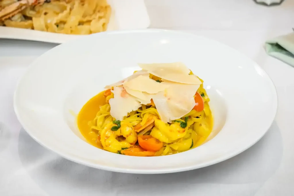 Plated creamy pasta with shrimp, cherry tomatoes, and Parmesan shavings.