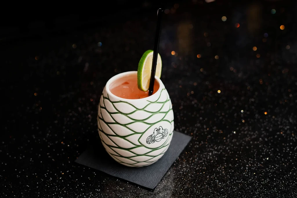 Reddish-orange cocktail in a patterned egg-shaped mug with lime.