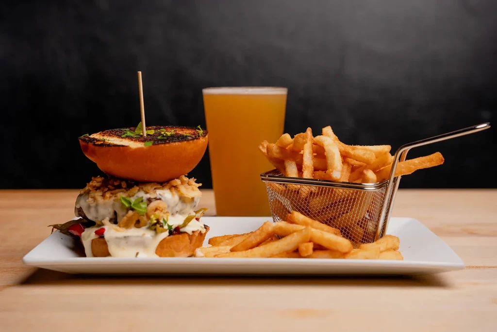 Gourmet burger with fries and beer, professionally plated on wood.