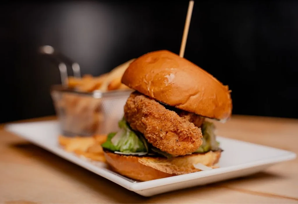 Golden fried chicken sandwich with lettuce and basket of fries.