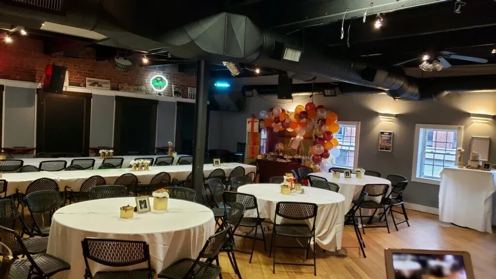 Rustic industrial event space with white tables and a vibrant balloon arch.